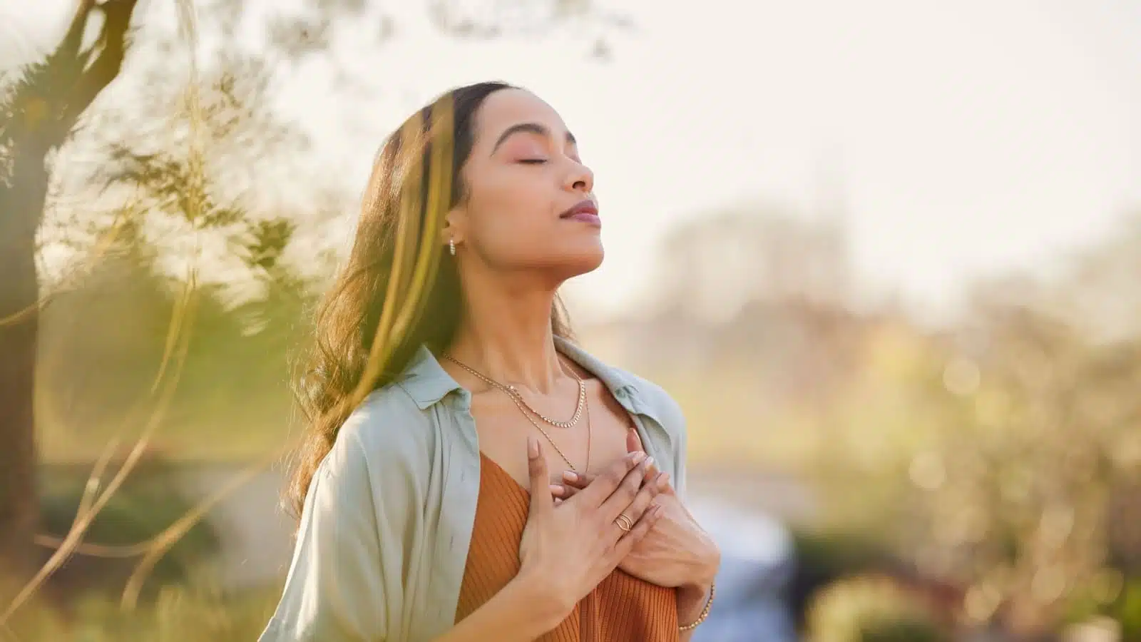 A woman stands outside with her hands on her chest and a grateful expression on her face.