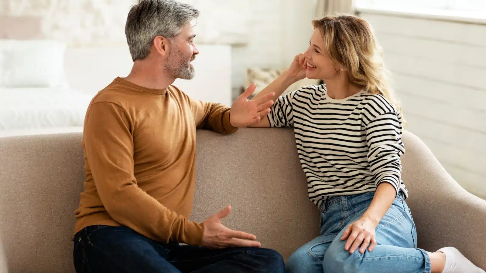 A happy couple sits on the couch talking.