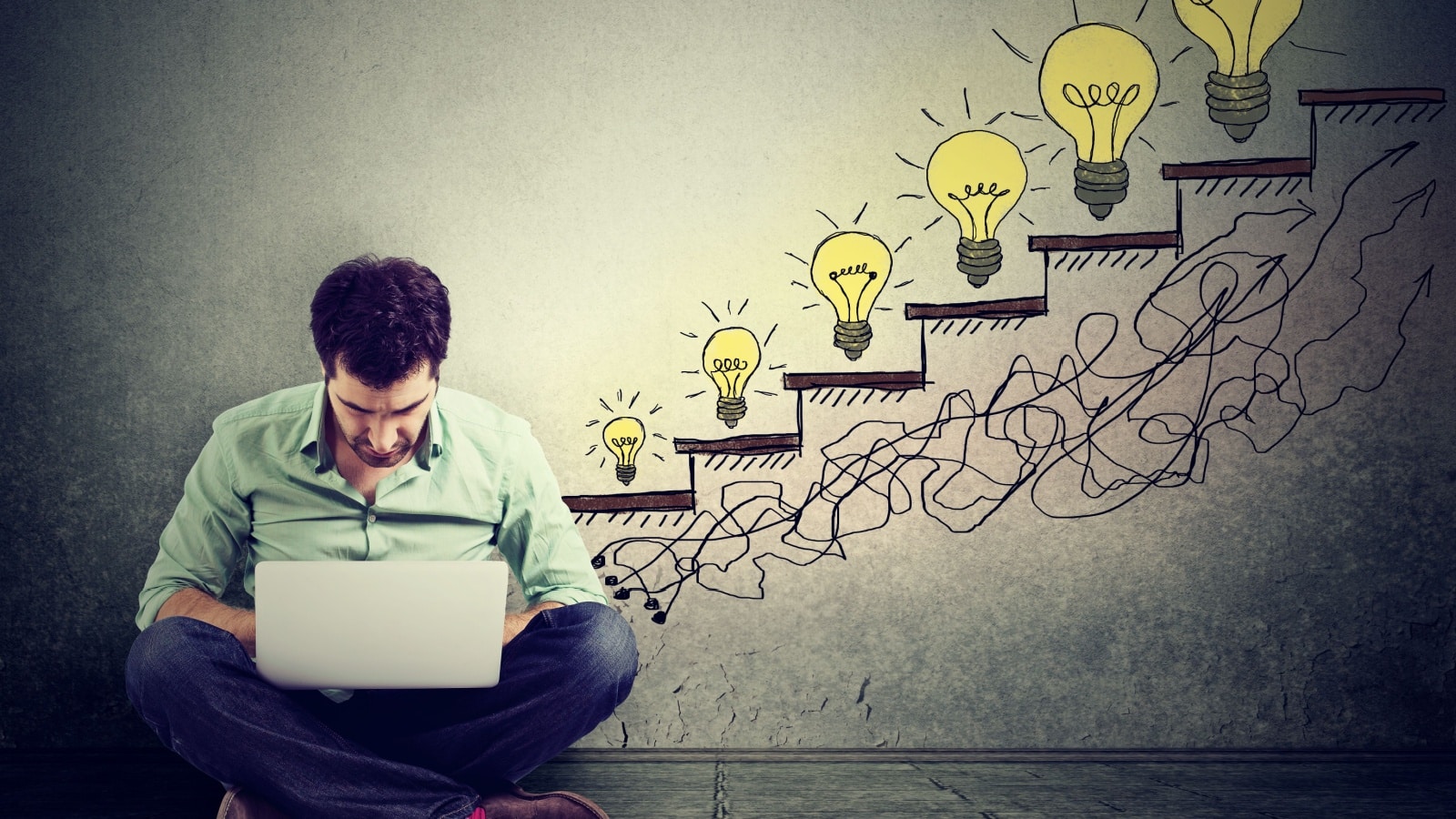 A man sitting cross legged at his laptop, planning his life. Behind him is a graphic of a staircase leading up, with glowing light bulbs at each step.