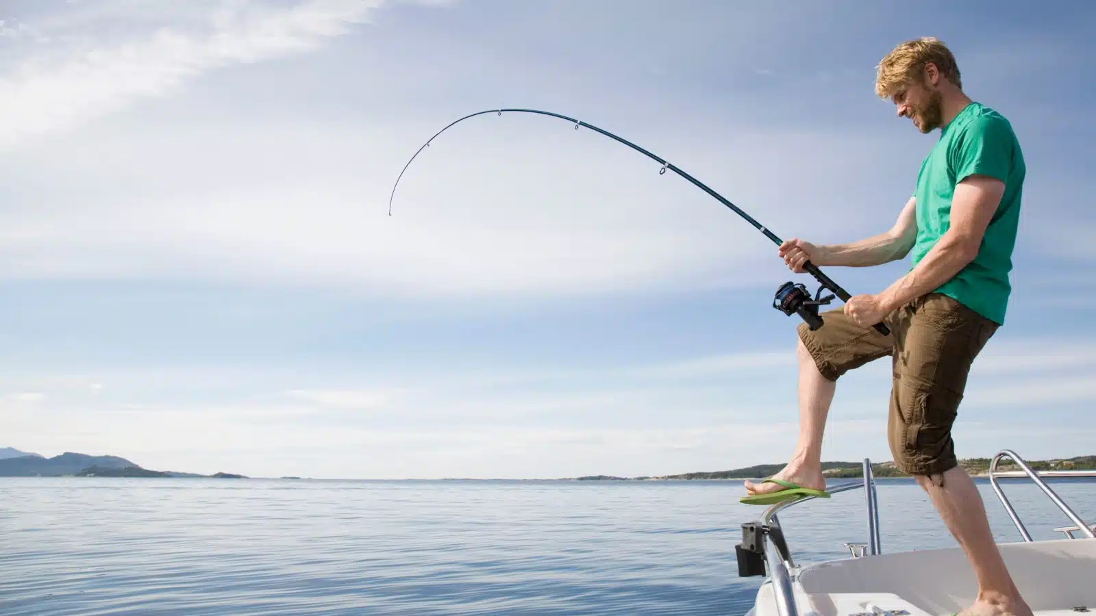 A man battles a large catch while deep sea fishing on a boat.