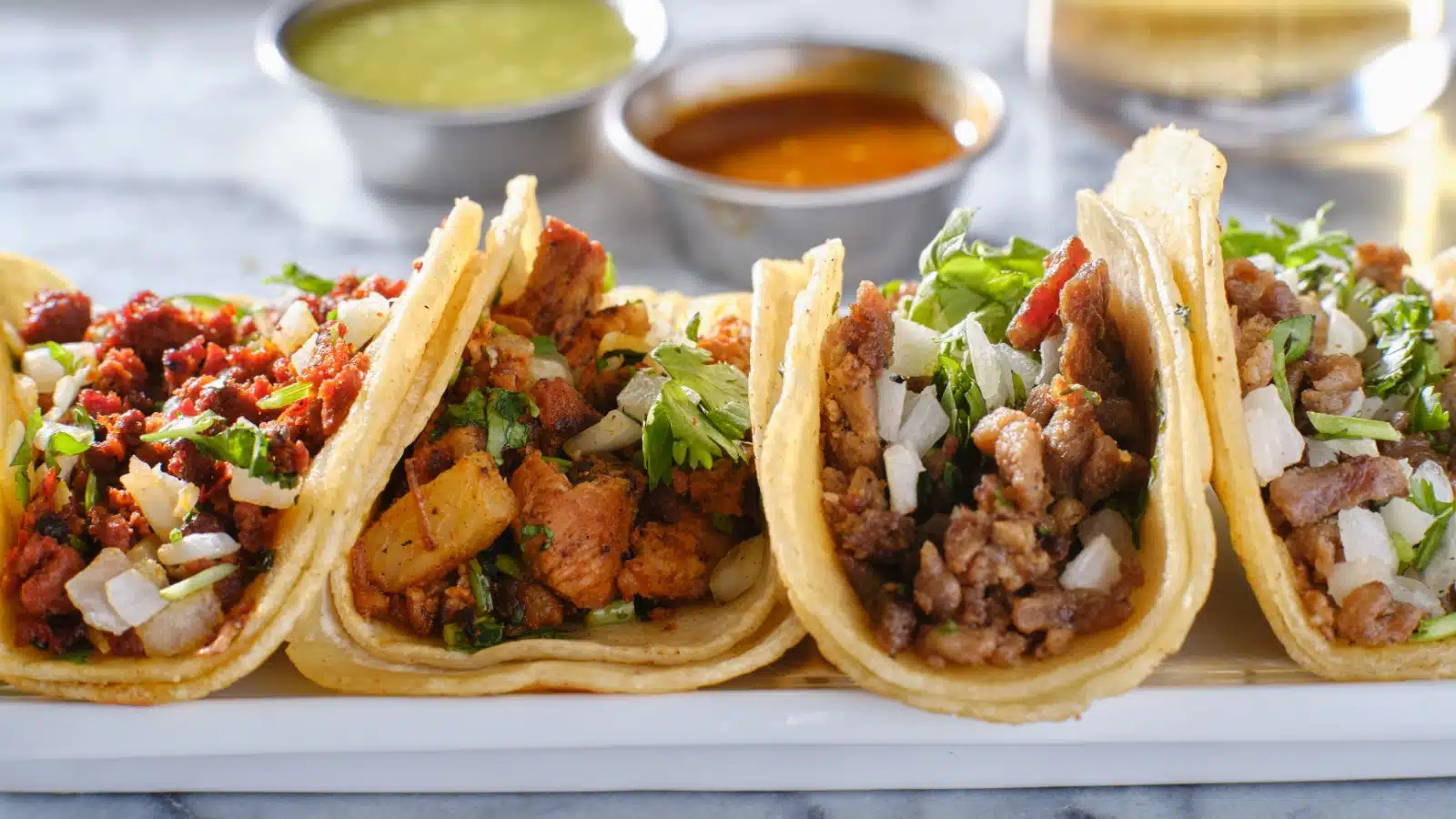 A plate with four different Mexican street tacos, one of them has potatoes.