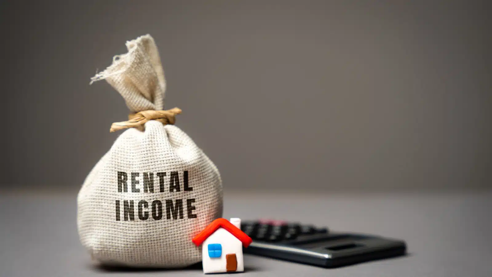 A money bag labelled "rental income" sits next to a tiny model home and a calculator.