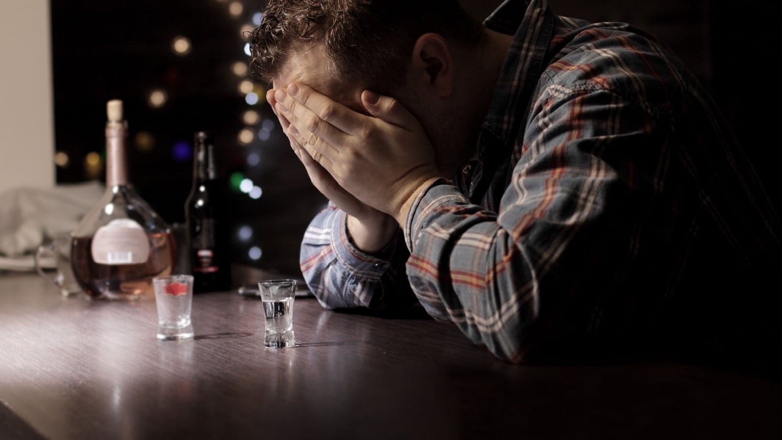 A sad man sits at a bar with his head in his hands.