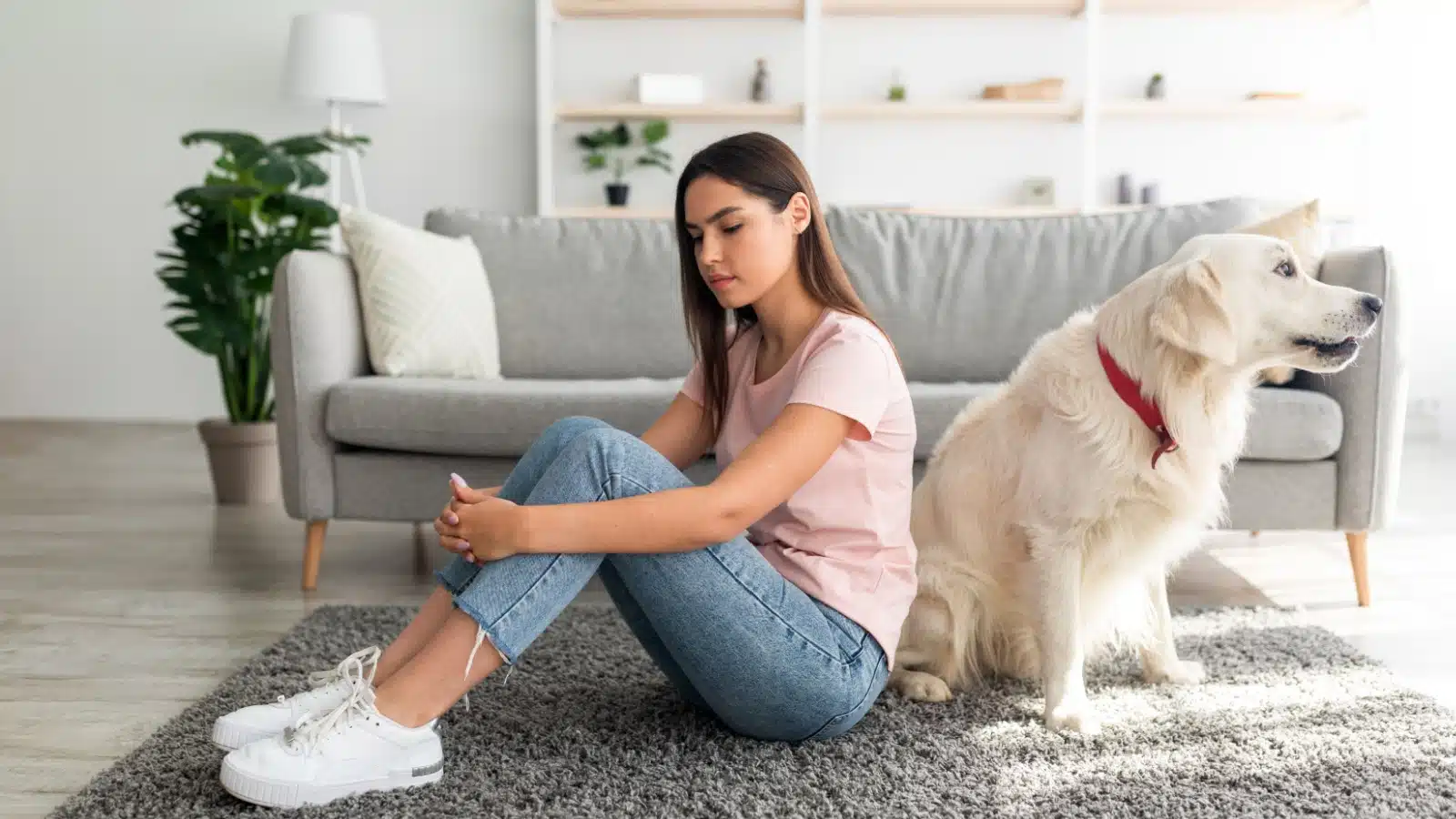 A sad woman sits with her back to her dog.
