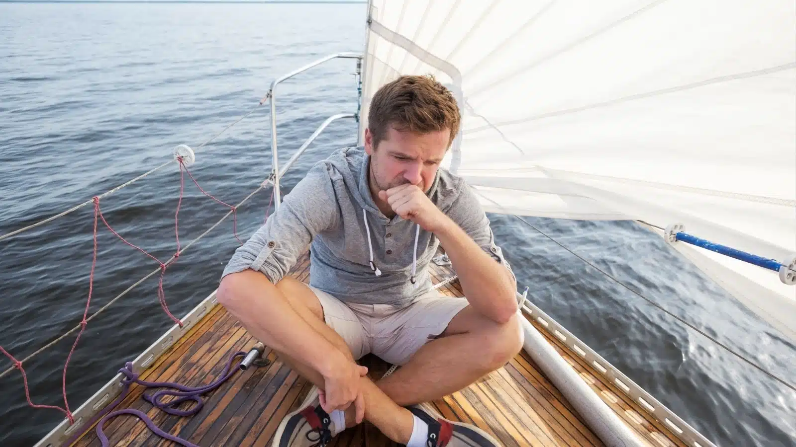 A seasick man sits on the deck of a boat.