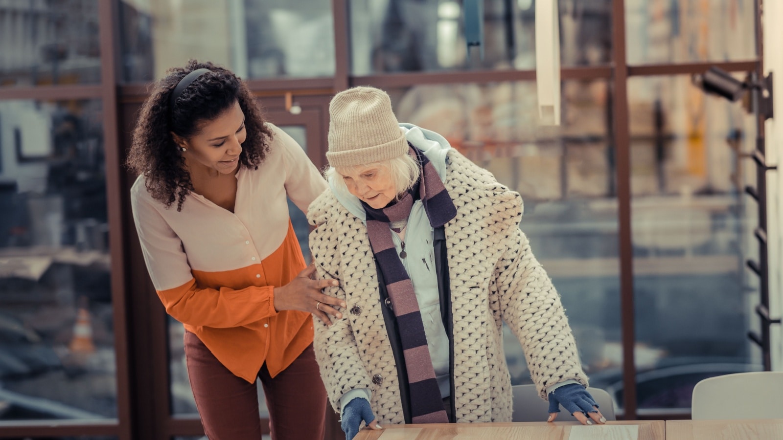 A middle aged woman helps a senior woman balance while walking outside.