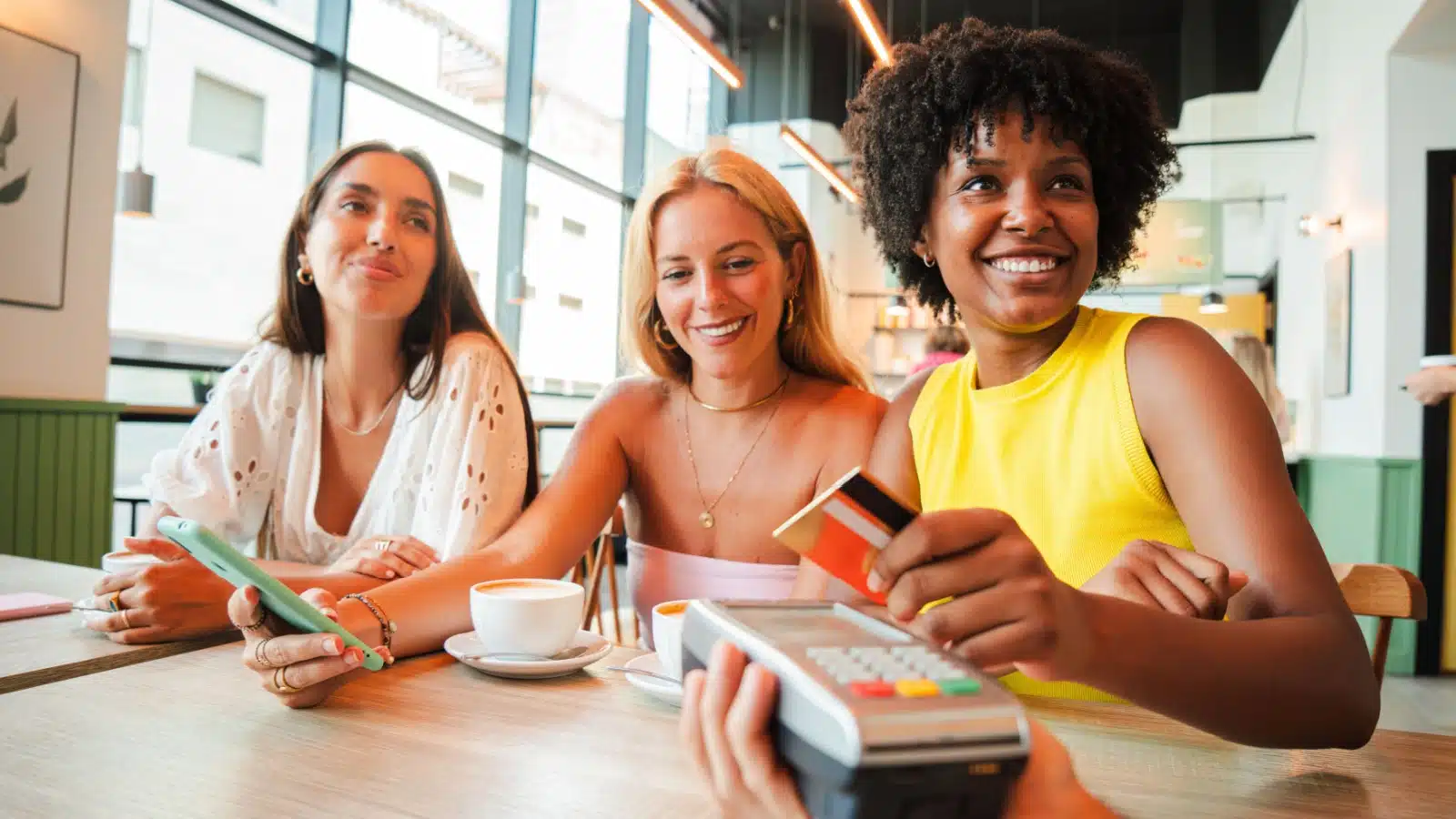 A happy woman buys her friends coffee to represent spending money on what you love.