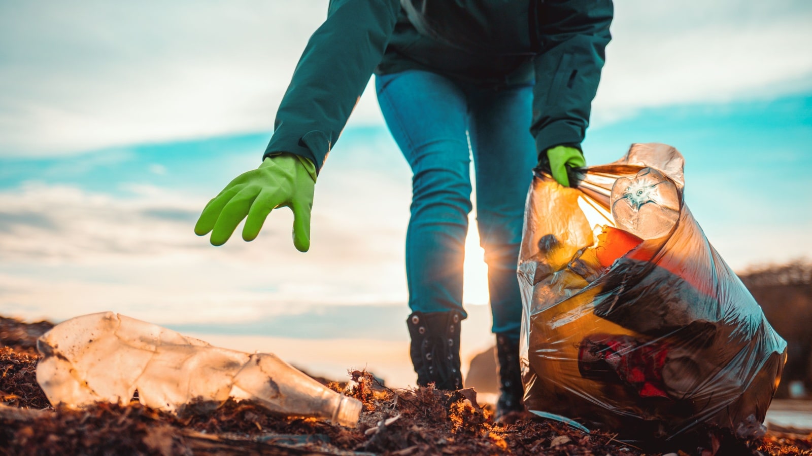 A volunteer reaches to pick up a bottle while on a clean up project.