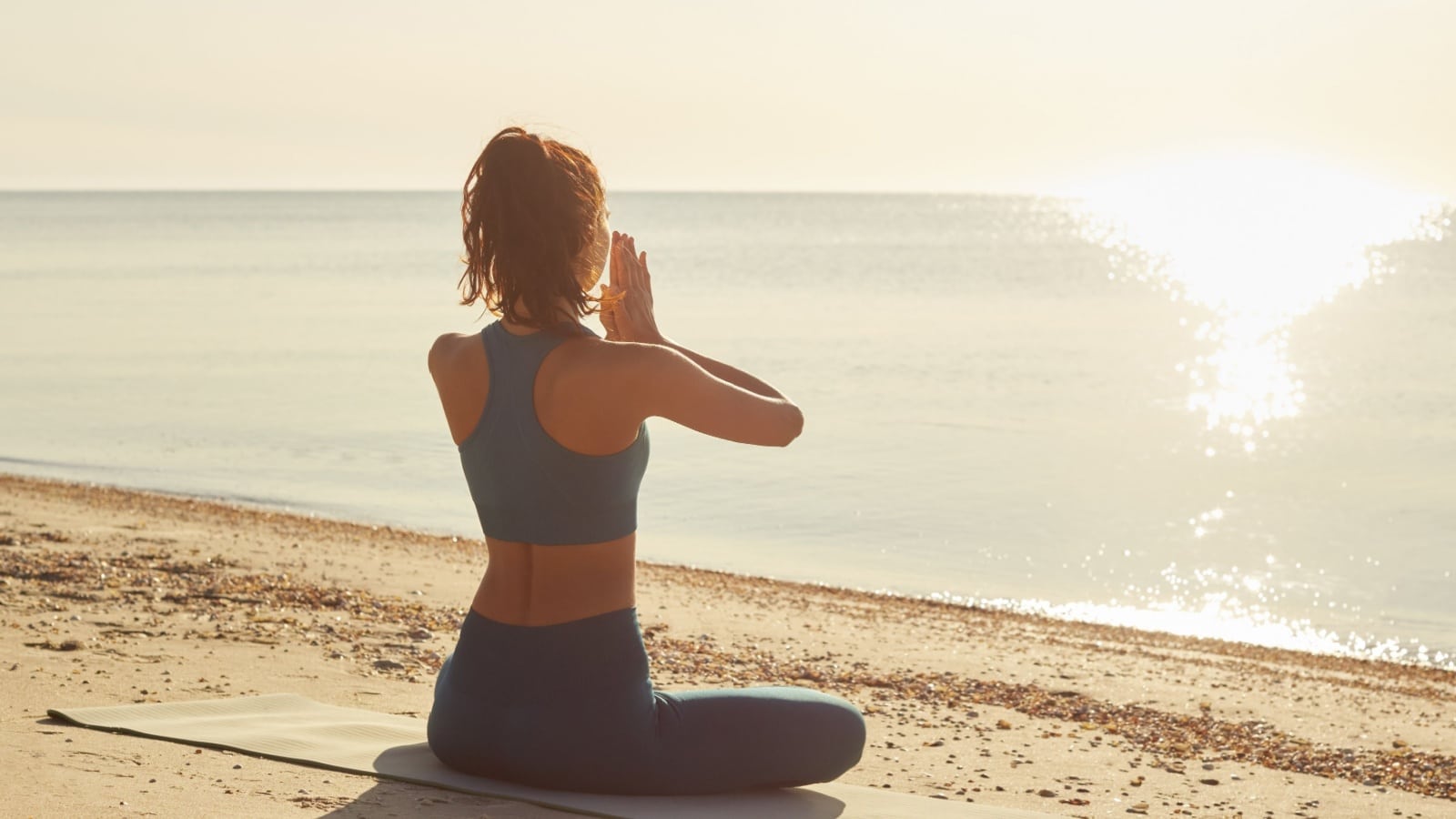 A woman practicing yoga on a beach to represent enhancing your mental health.