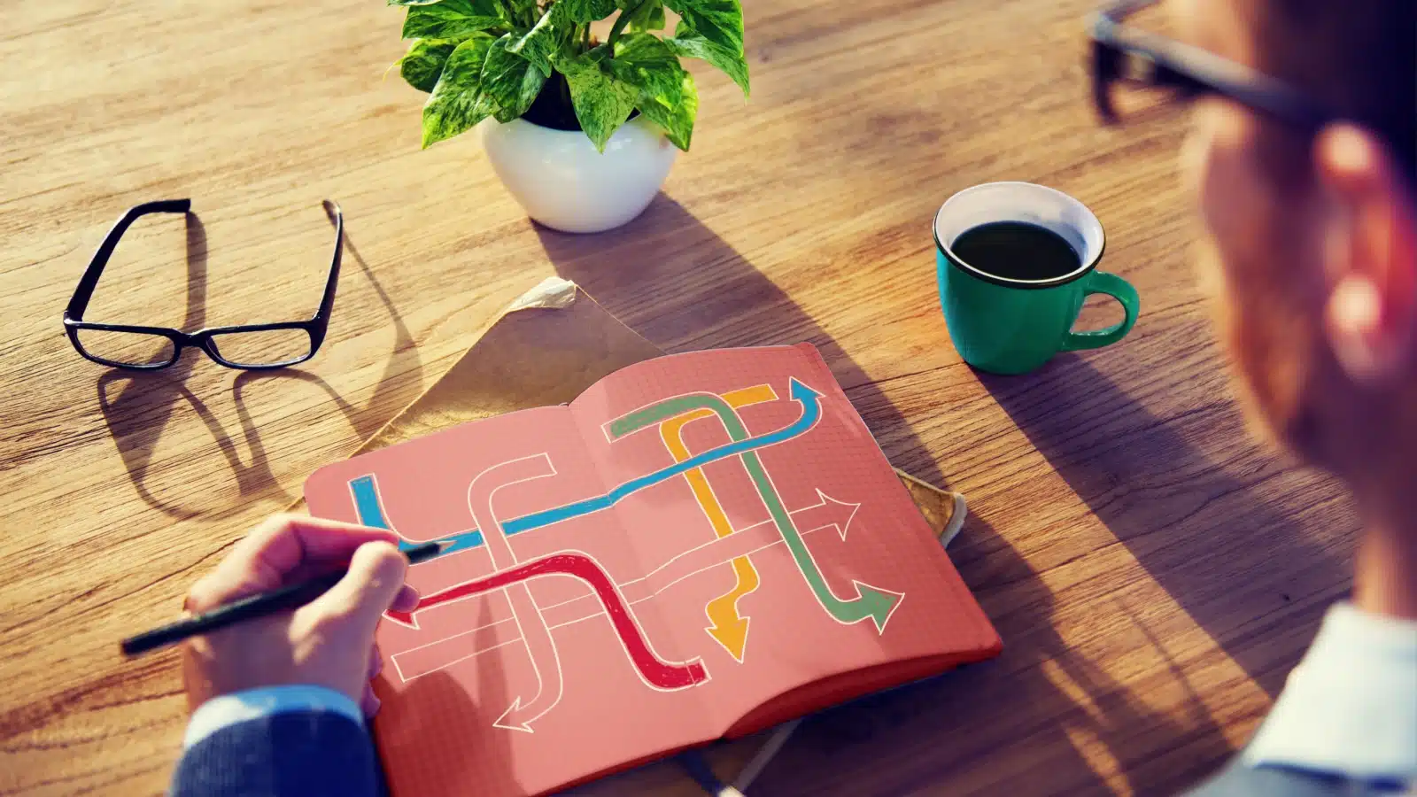 A man draws a diagram in his journal of arrows outlining different paths he can take. The image represents someone deciding what they want out of life.