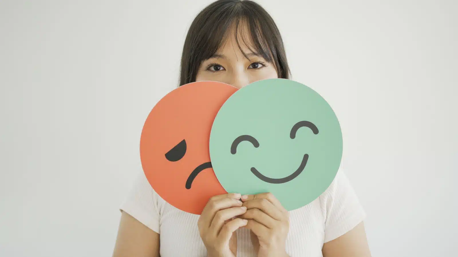 A woman holds signs showing a happy face and a sad face.