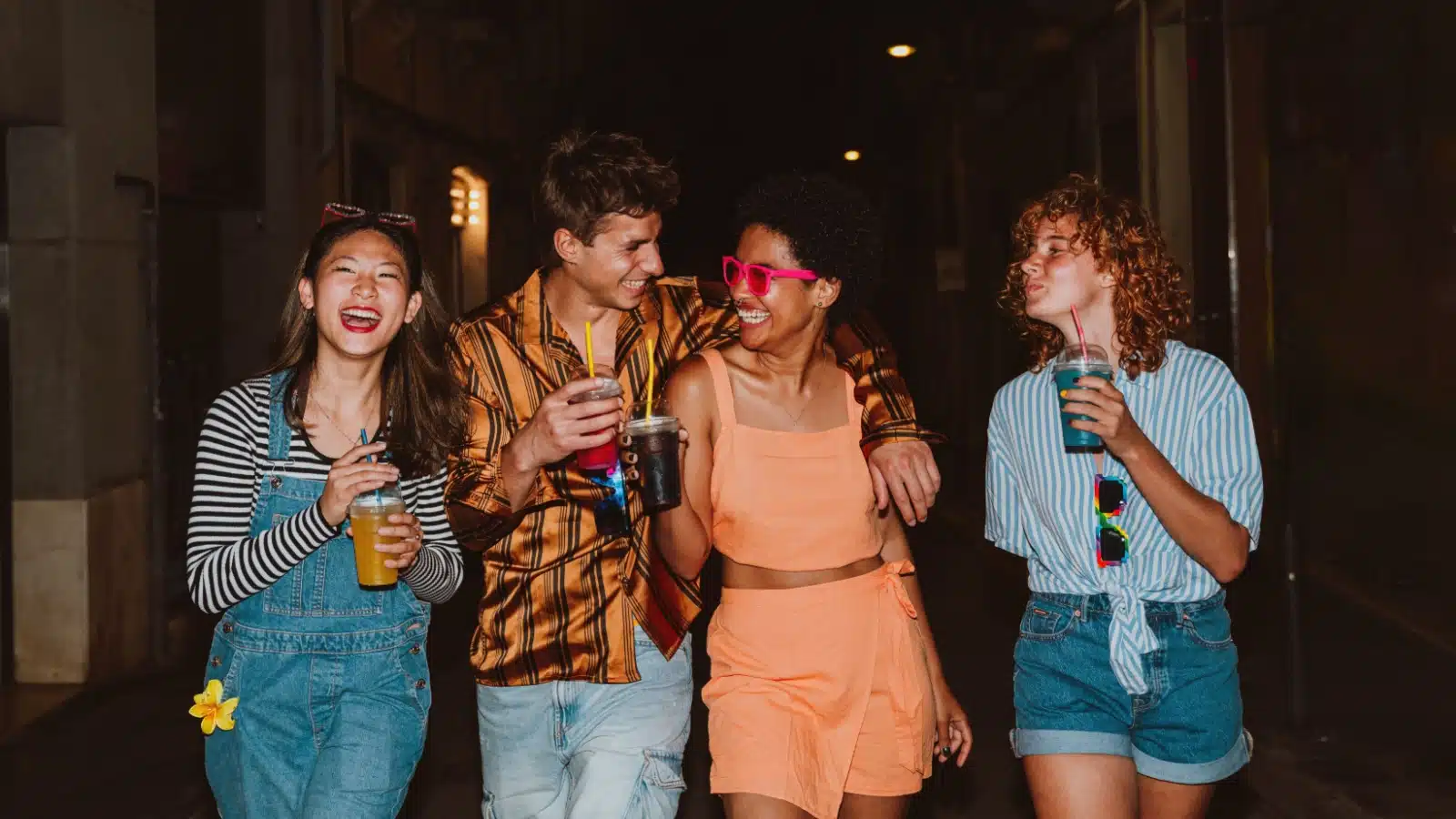Four friends walking down an alley after enjoying a night out. They're laughing, smiling, and having a good time.