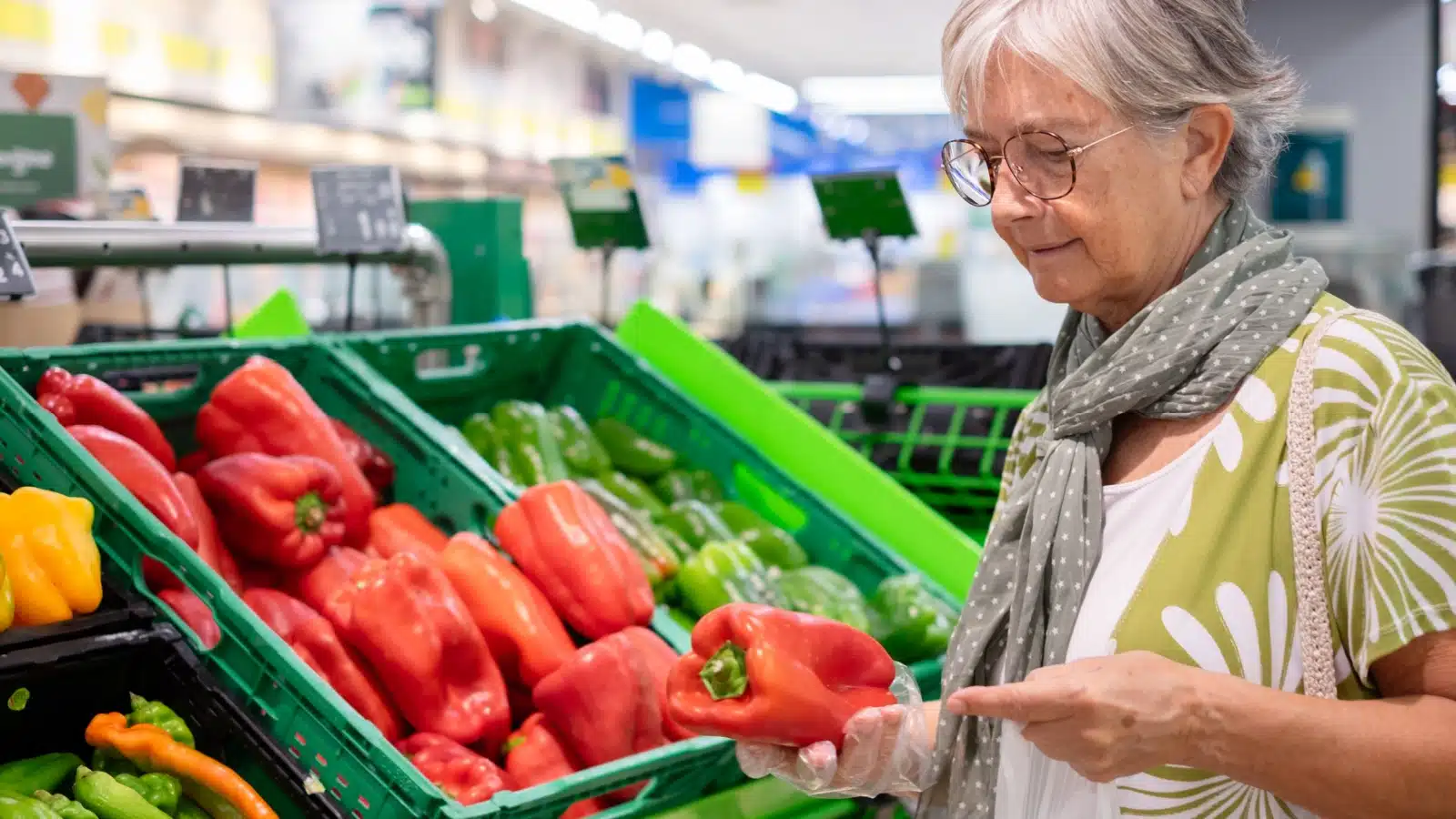 A senior woman in the vegetable aisle of the grocery store represents a $20 grocery budget.