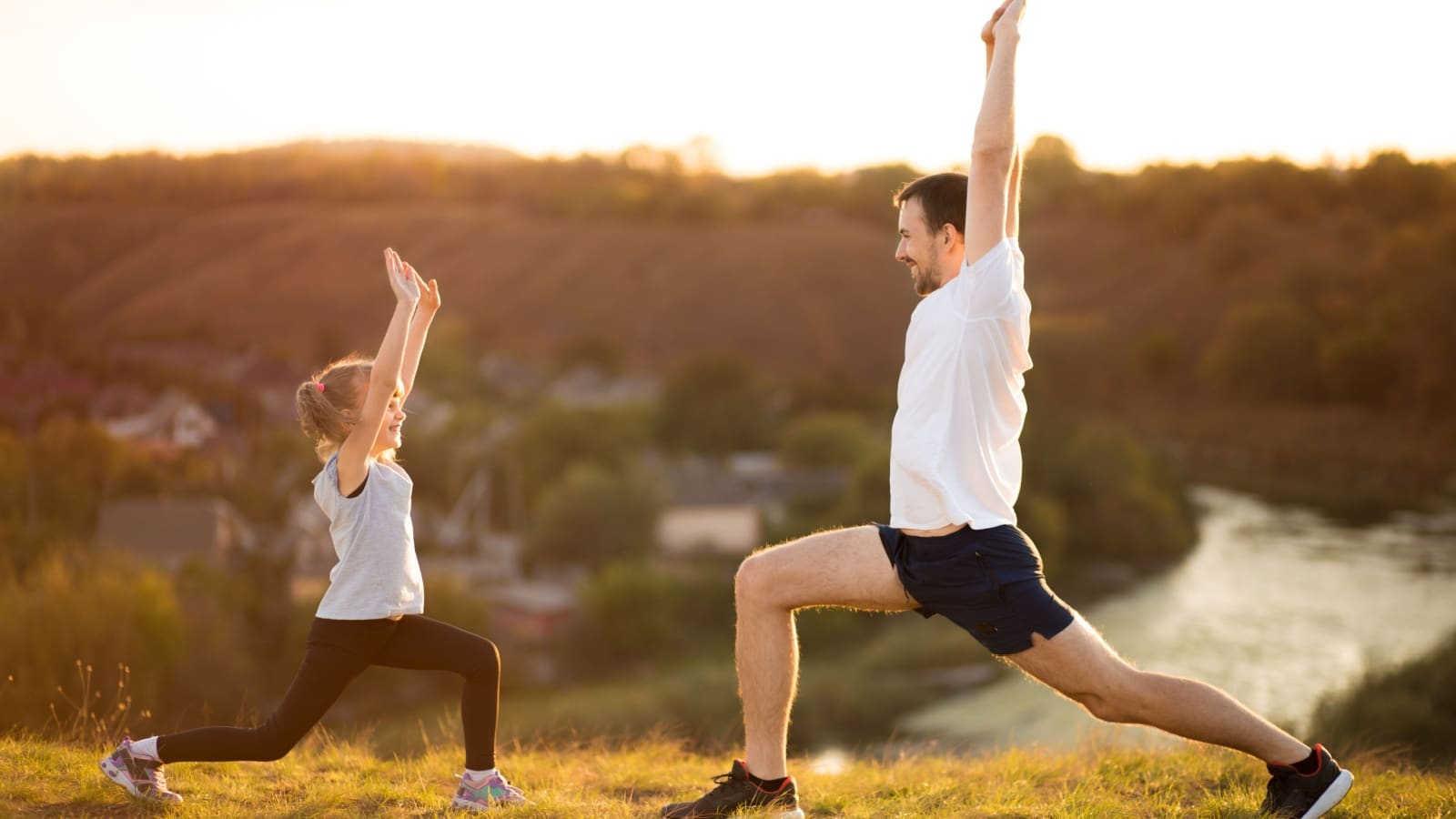 A father teaches his daughter healthy habits. They are outside stretching together.