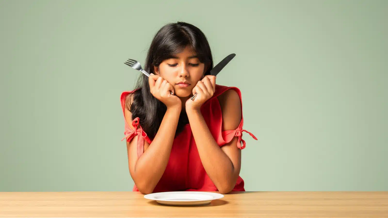 A hungry woman stares at an empty plate. She's skipping a meal because she can't afford to eat.