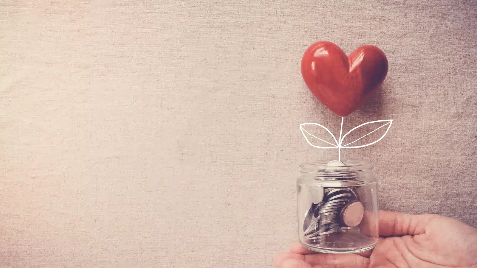 A hand holding a small jar of change with a little heart growing out of it.