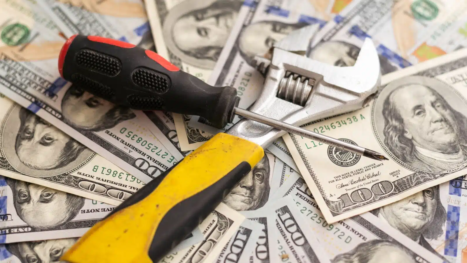 A wrench and screwdriver sit atop a pile of money to highlight that money is a tool.