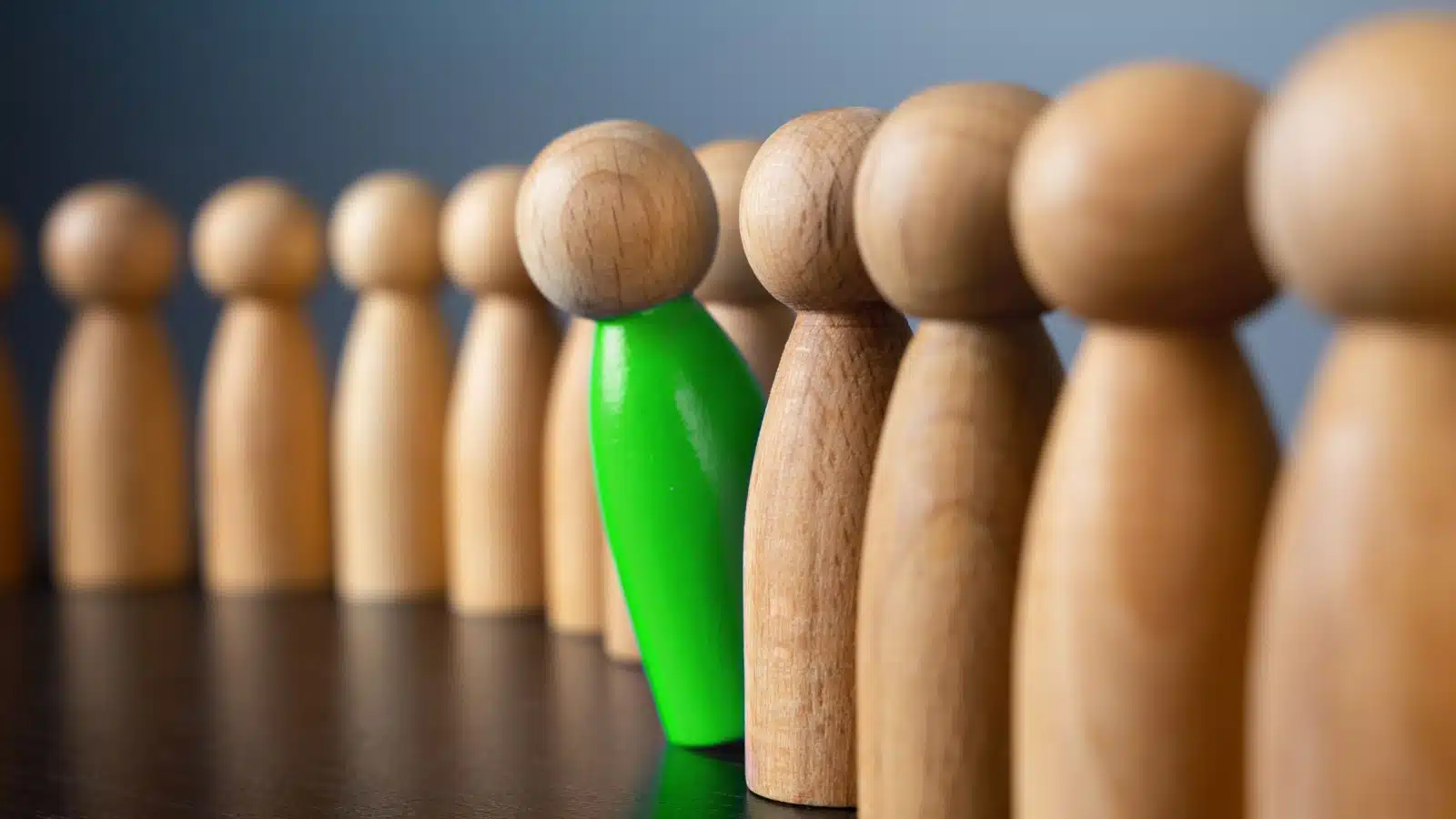 A green wooden cog peeks out of a line filled with bland wooden cogs.