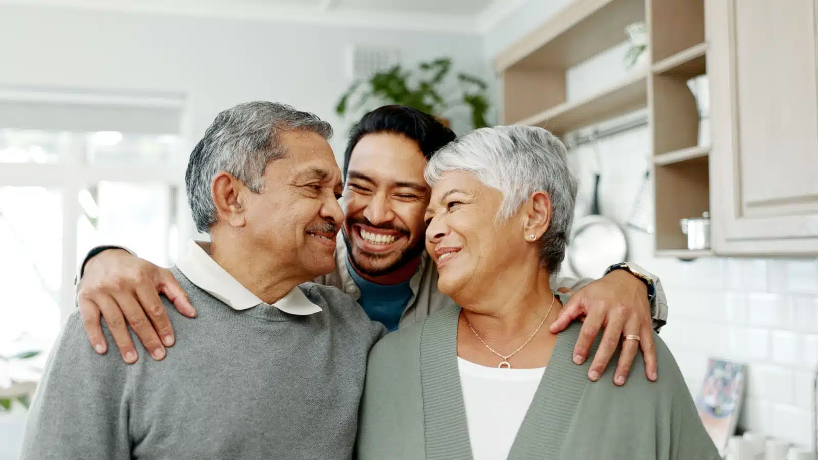 An adult son hugs his senior parents.