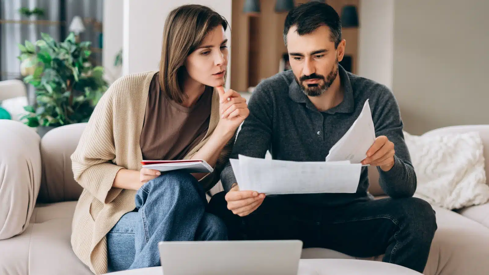 A couple sits on the couch reviewing paperwork together.
