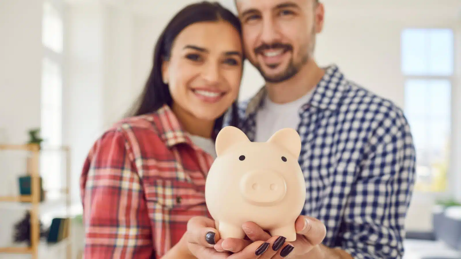 A couple holds a piggy bank out to represent saving money.