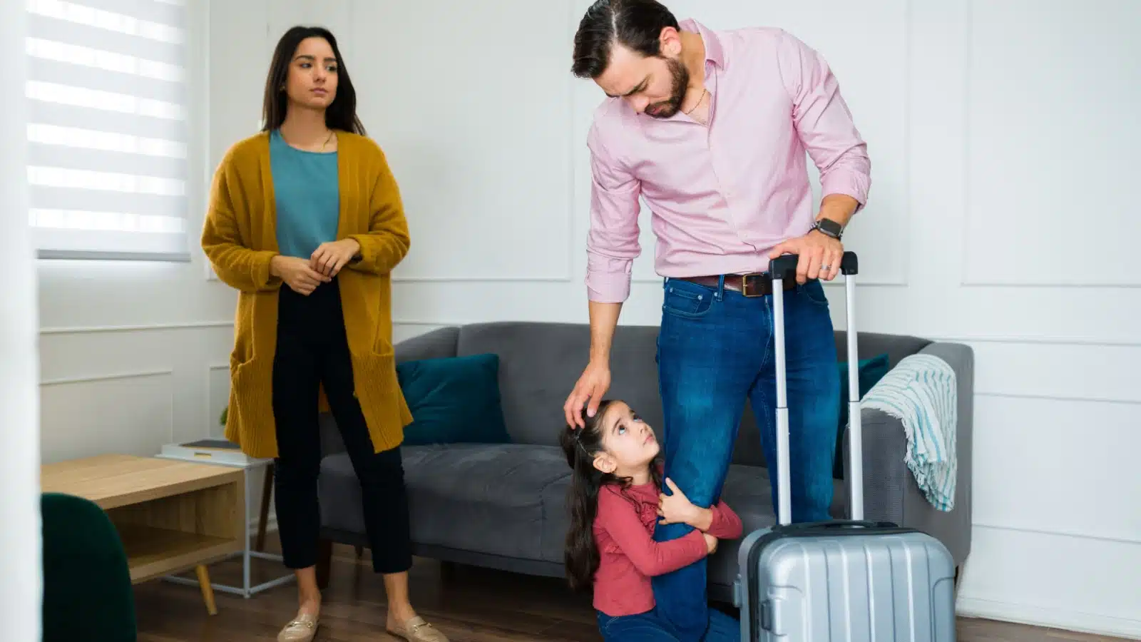 A father leaves the home as the small child grabs his leg as if begging him to stay. An unhappy wife watches in the background.