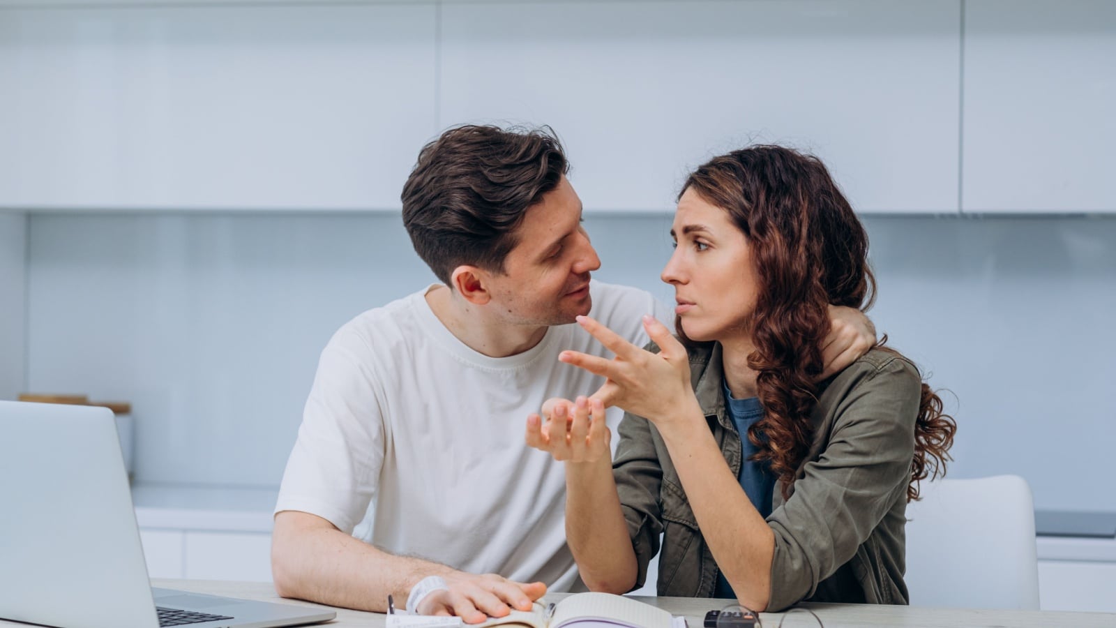 An uncomfortable scene with a couple discussing finances. The woman looks tense, and the man has his arm around her head in a controlling way.