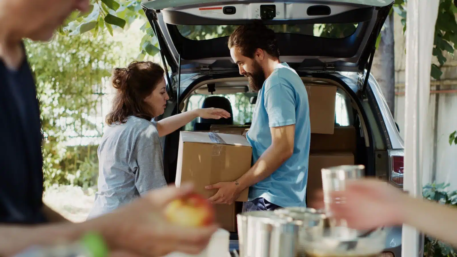 A volunteer helps a woman load a box of food into her car at a food bank.