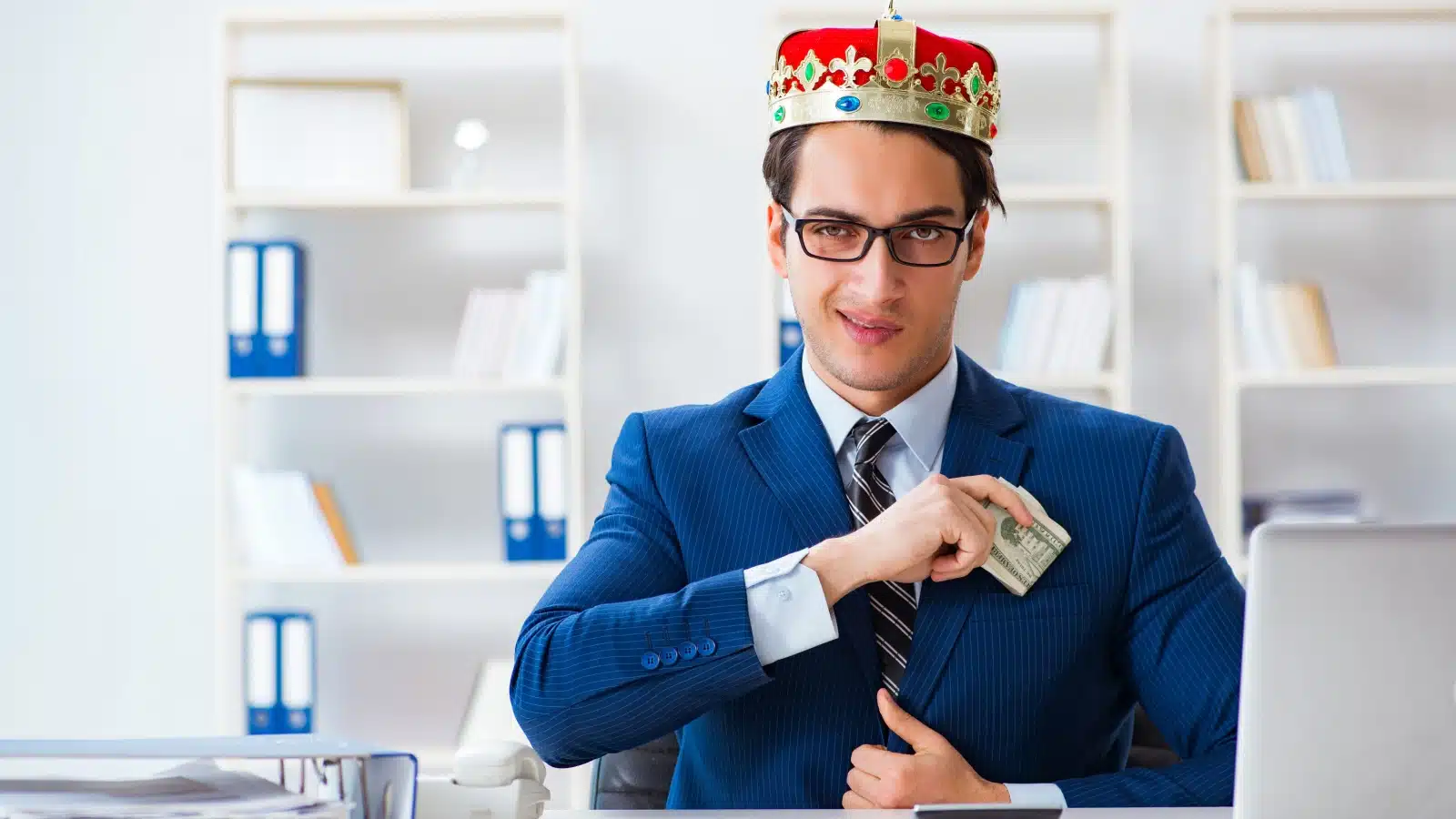 A greedy businessman wearing a crown slyly stuffs money into his pocket.