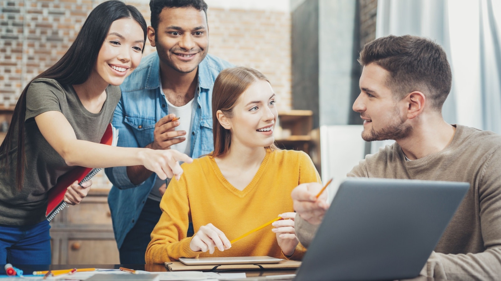A diverse group of young adults working together around a computer to represent interpersonal skills.