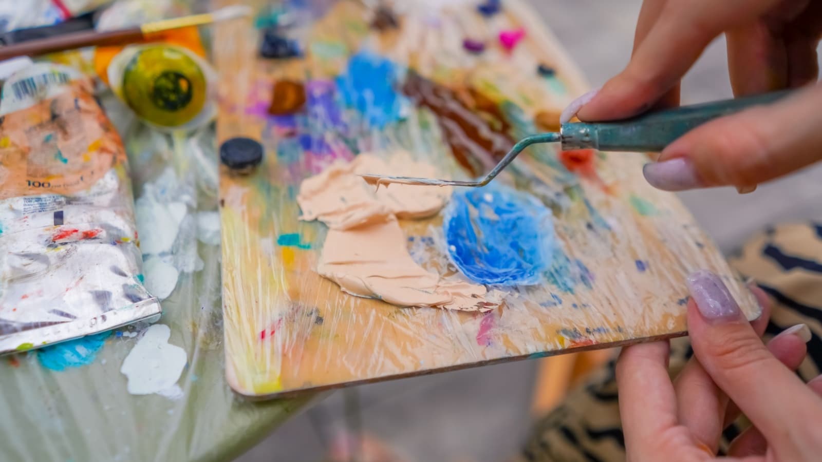 Close up of an artist's palette where she's mixing a light shade of orange, neutralizing it with blue.