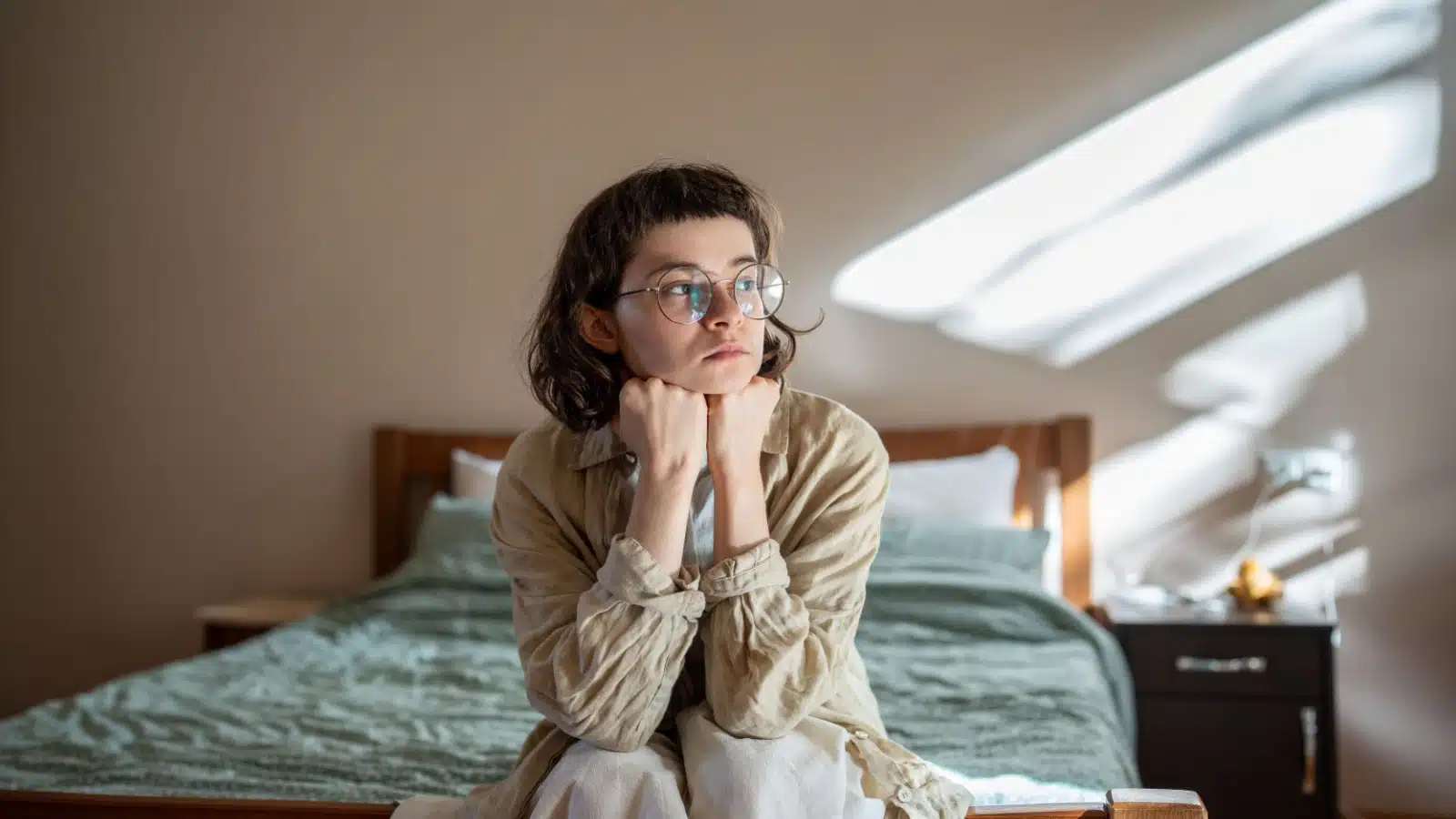 A sad lonely woman sitting on a bed to represent how society lies to women and prevents us from living authentically.