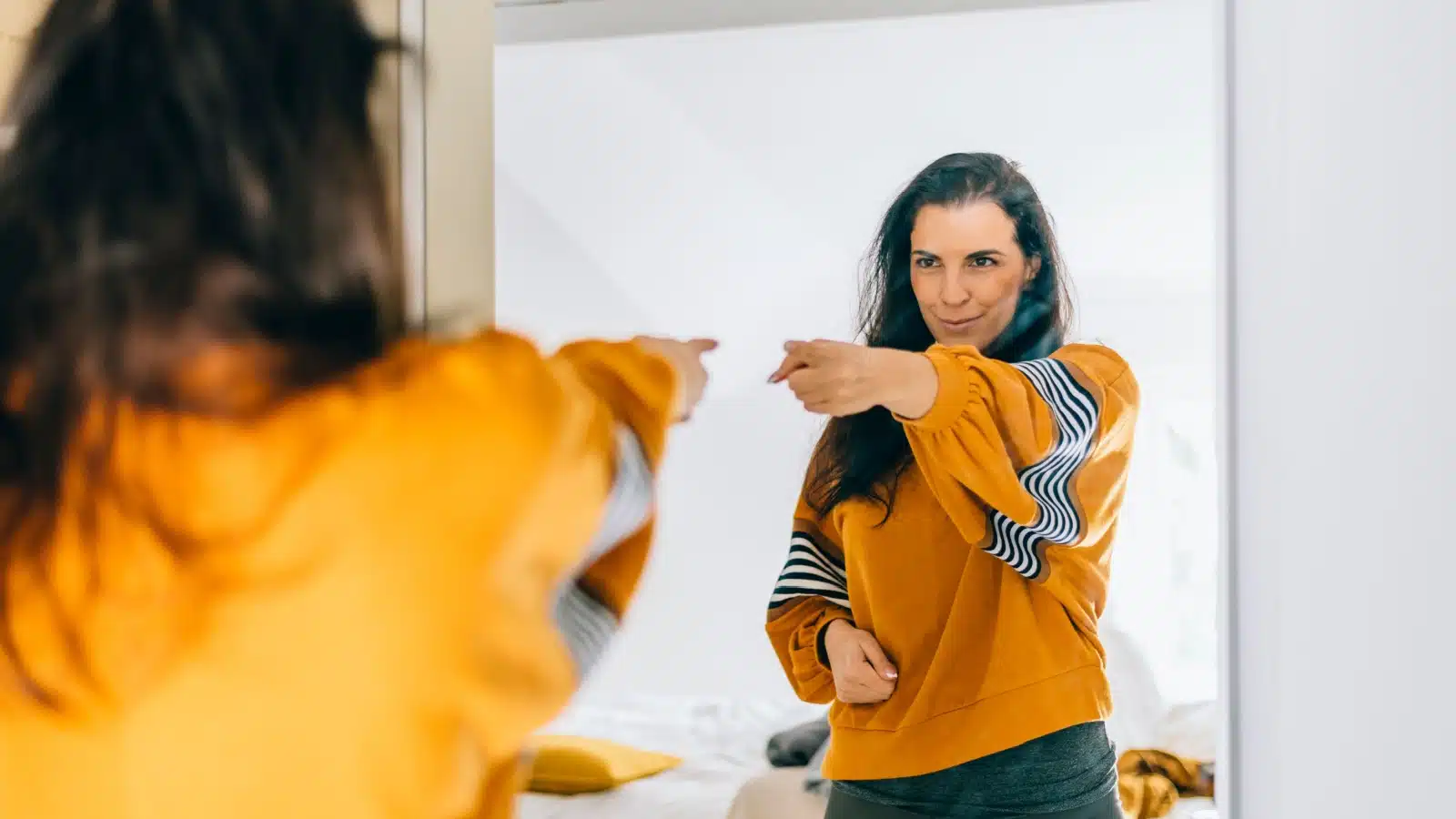 A smiling woman points to herself in the mirror. She's building her self-esteem and sense of self-belief.