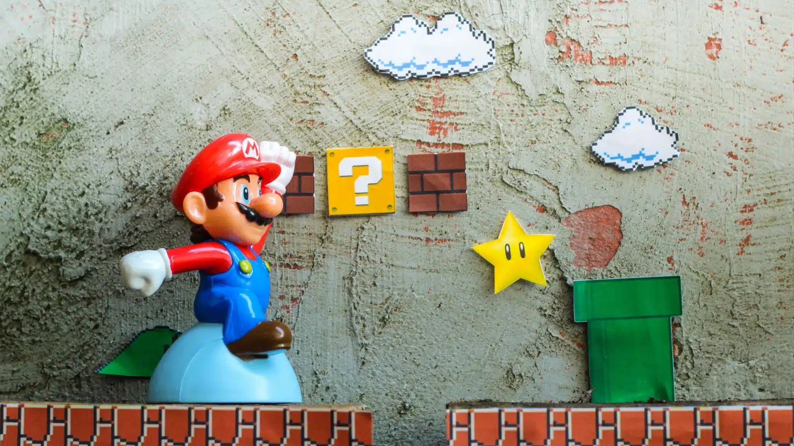 Cut out artwork showcasing Super Mario bros. The Mario figure looks 3D, but he's exploring a flat side scroll world from the original games. 