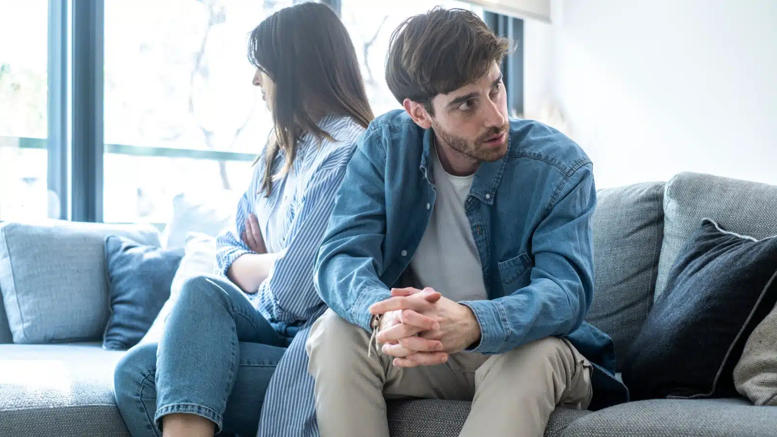 A couple sits on the coach after a fight, ignoring each other.