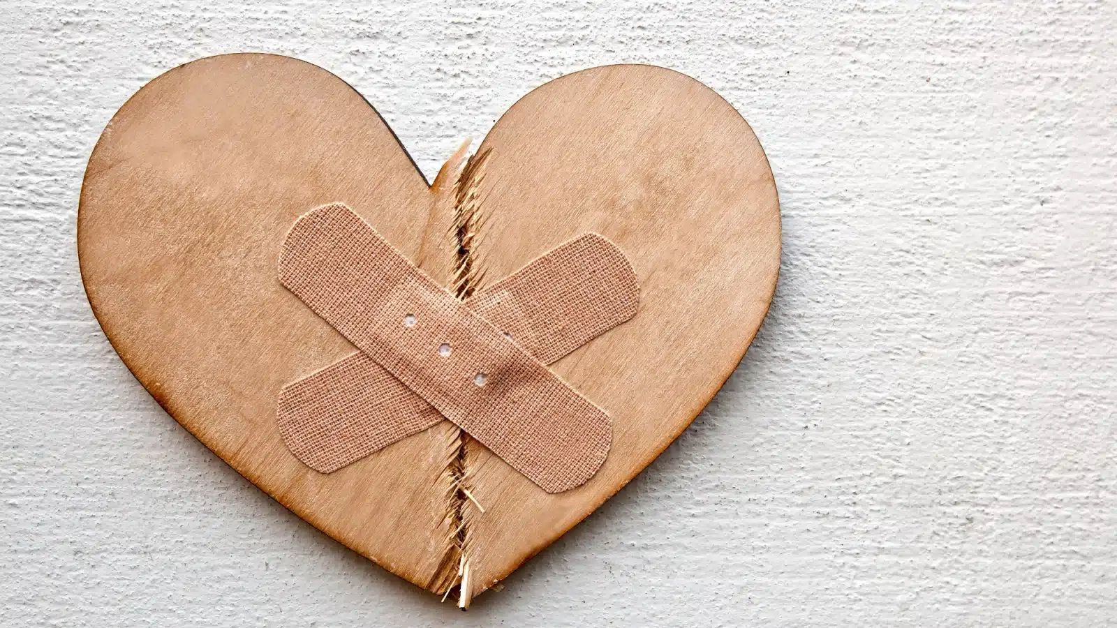 Forgiveness concept photo. A wooden heart is broken in half,, but patched together with band aids.