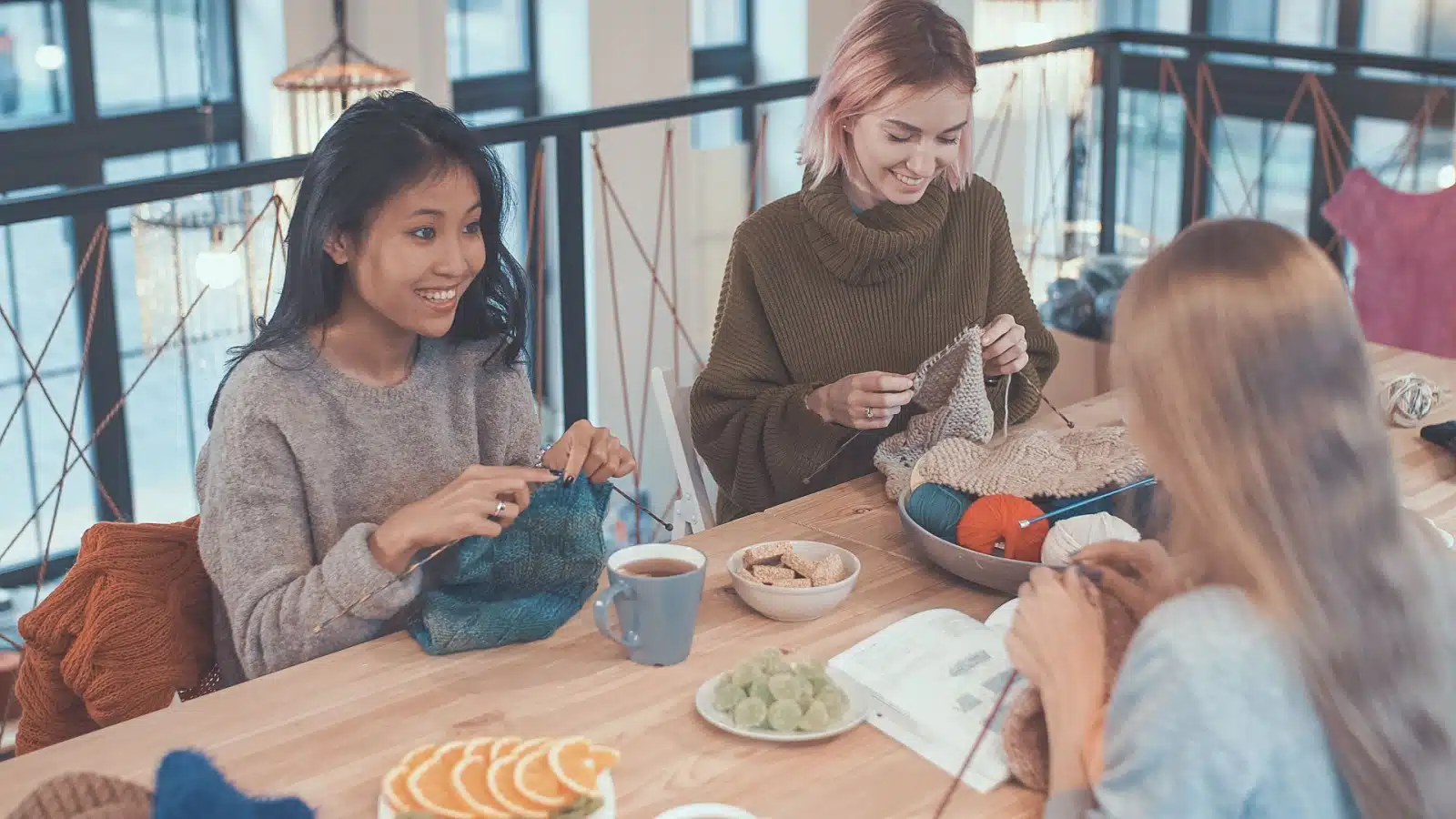 A group of friends sits together at a table while knitting.