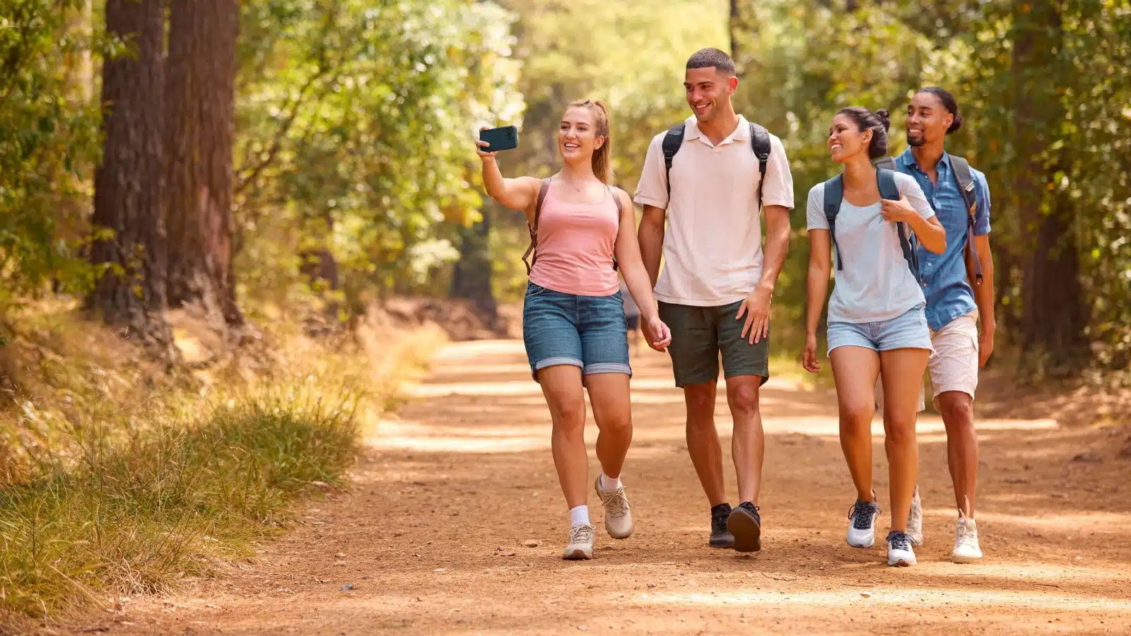 A group of friends takes a selfie as they hike through a forest.