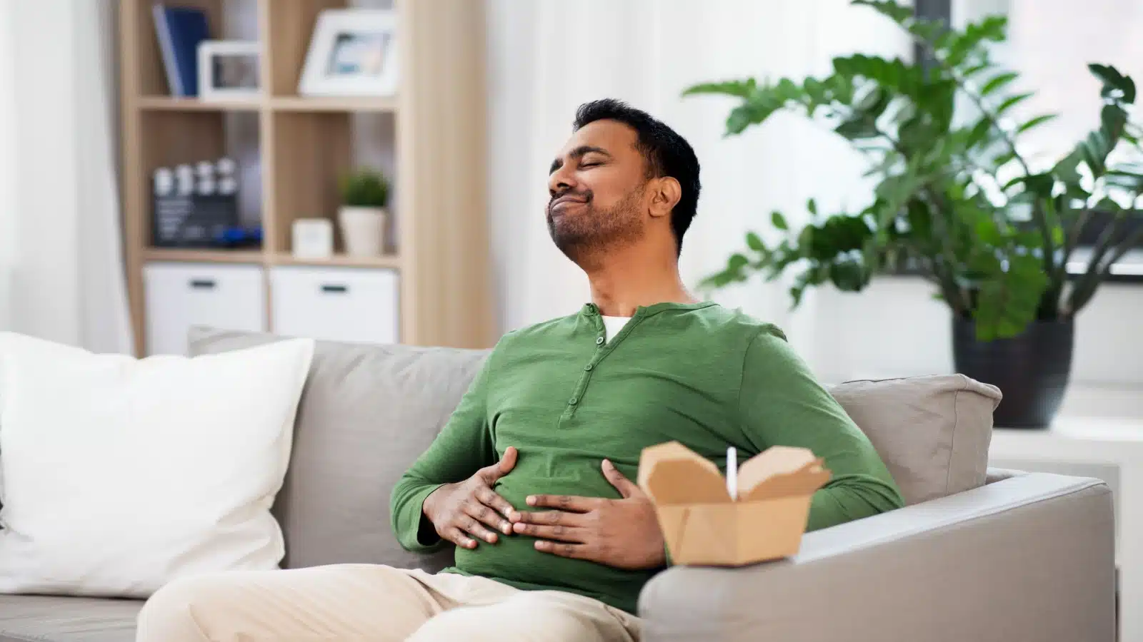 A man pats his stomach after eating. He's full and satiated after a good meal.