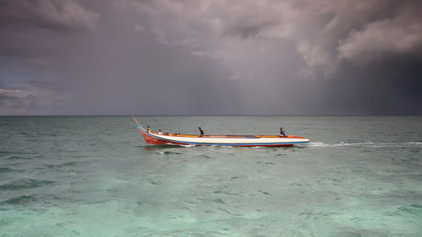A long boat on the sea with a massive storm on the horizon.