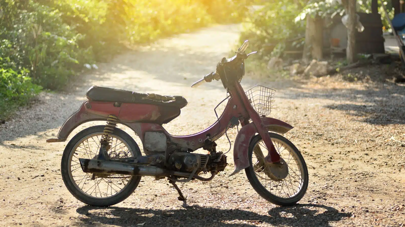 An old moped scooter stands on a dirt road.