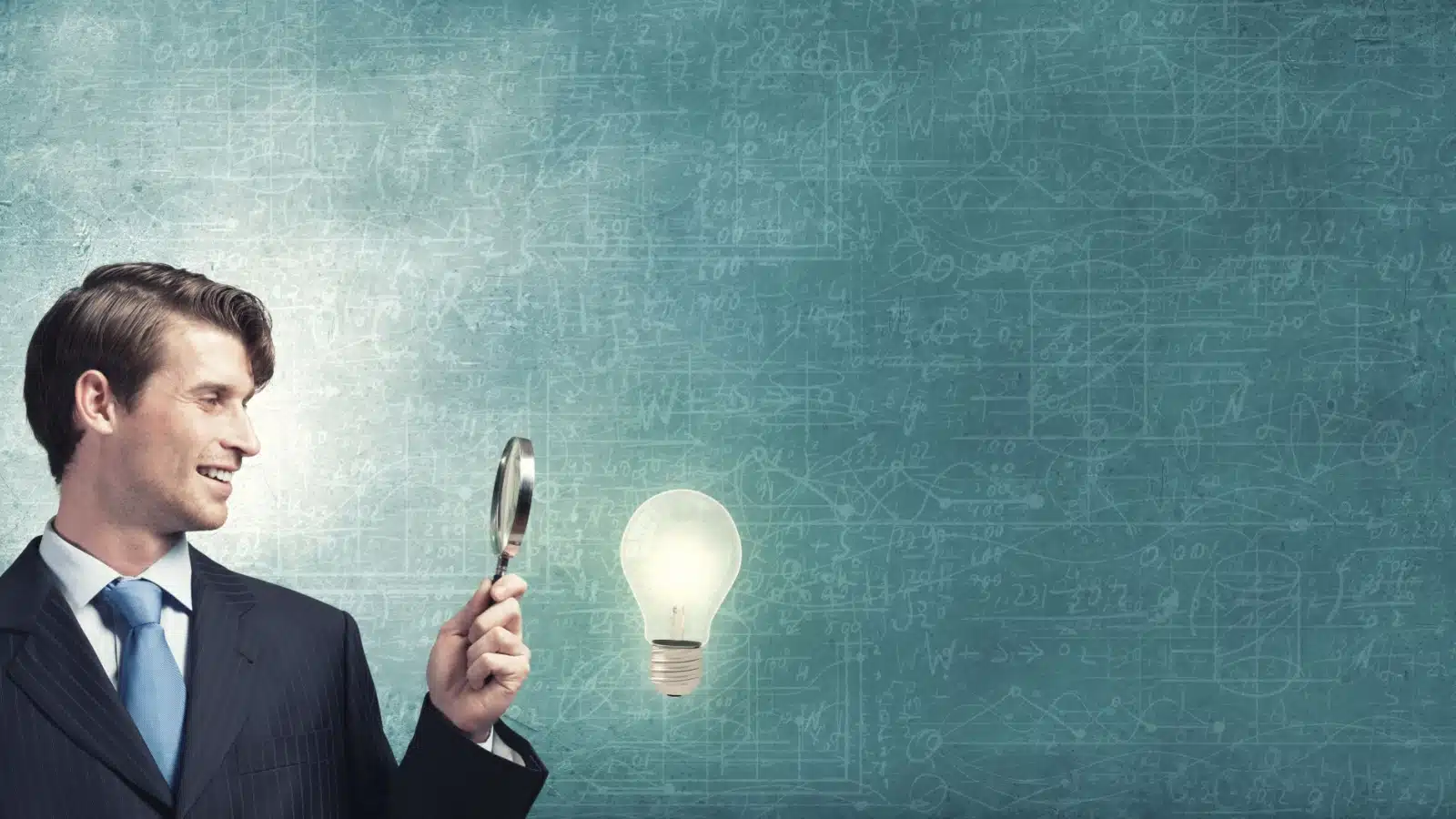 A smiling man holds a magnifying glass up to a light bulb that's shining in front of a chalk board with equations on it, to represent deep diving into your niche hobby.