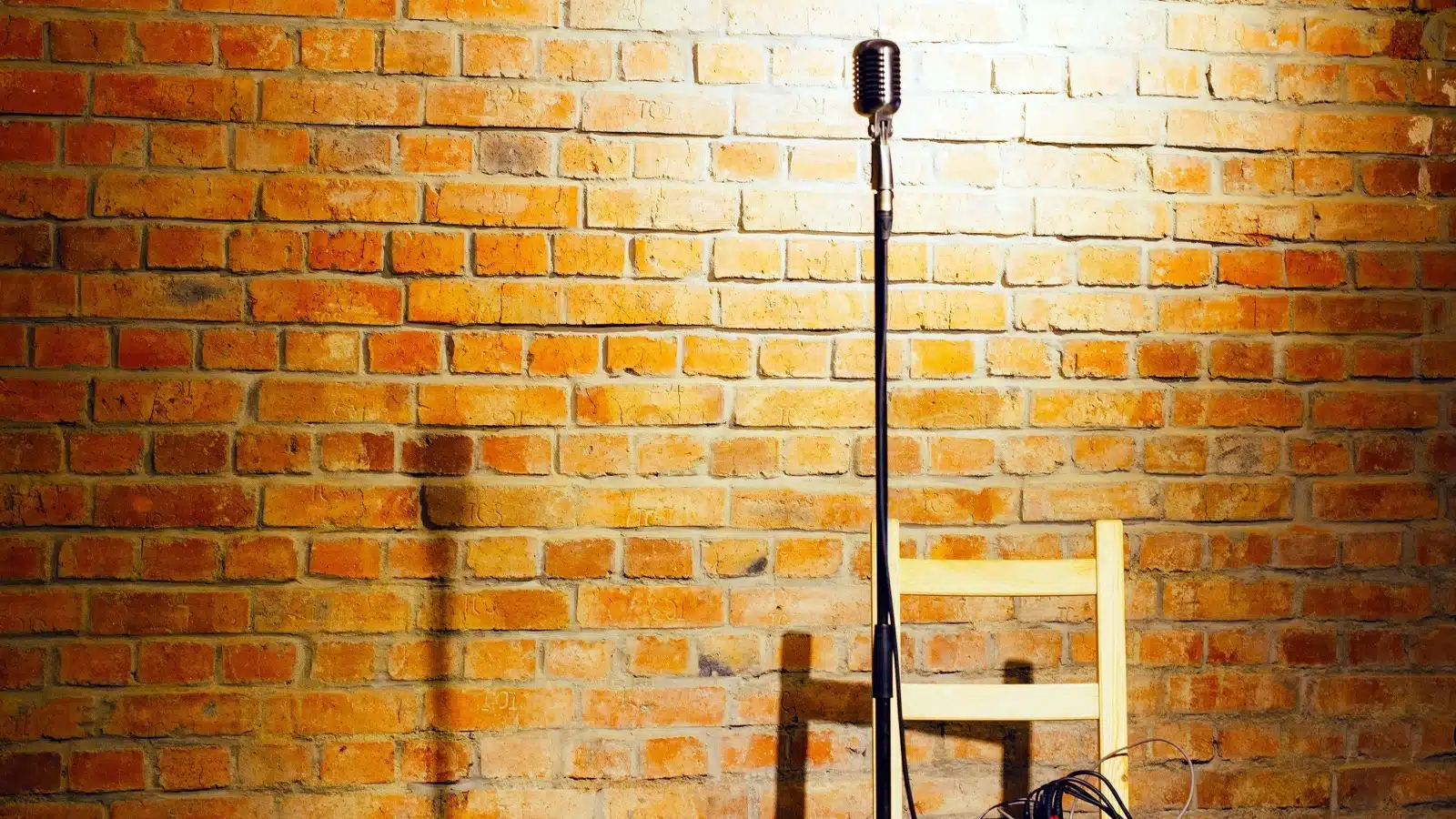 A microphone stands alone next to a brick wall, ready for open mic night.