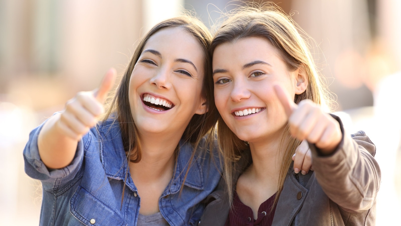Two women smiling and giving the "thumbs up" sign to show they have a positive attitude.