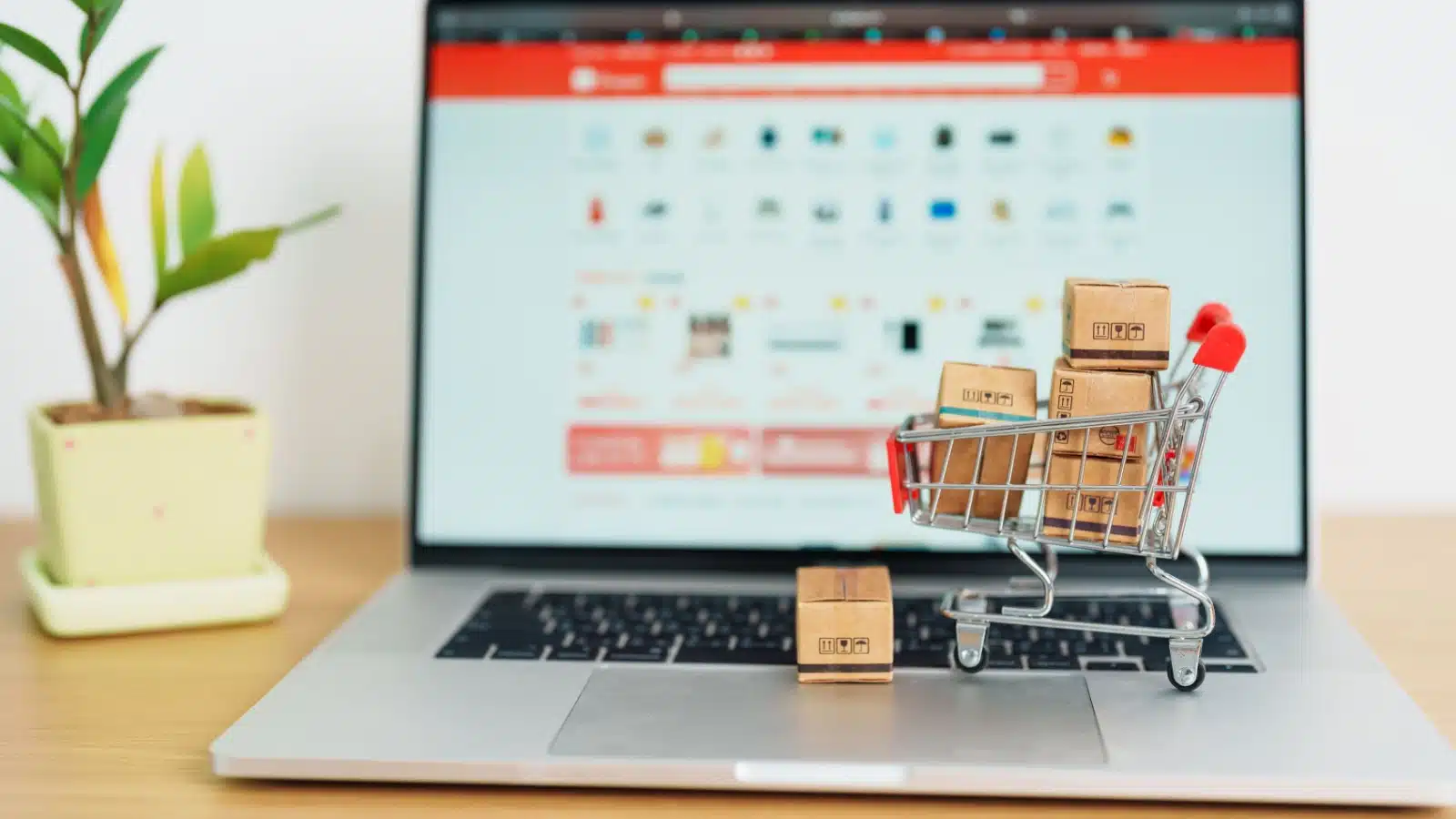 A model shopping cart filled with tiny boxes rests on a laptop to represent buying and selling online.
