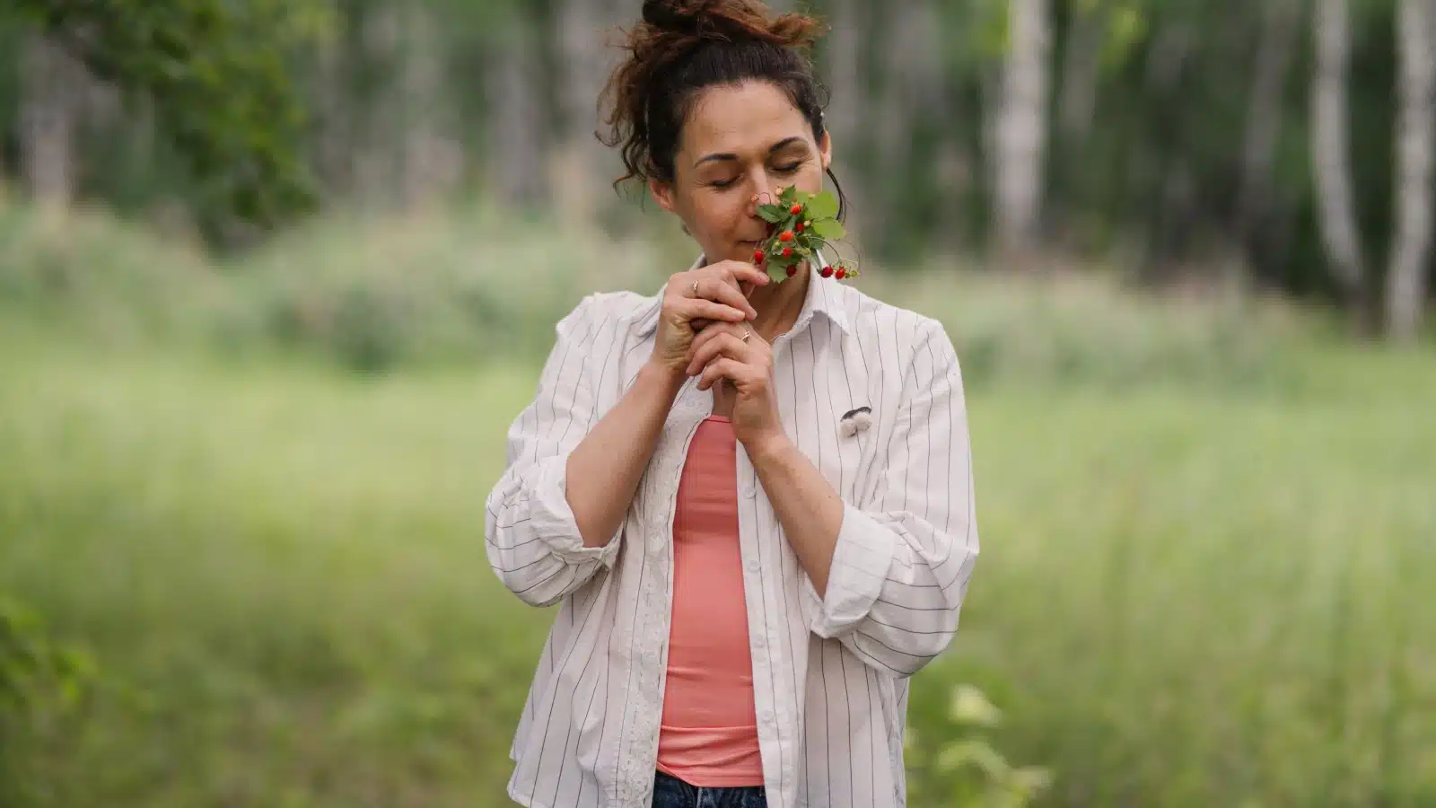 A happy woman in a field indulges in the scent of fresh berries.