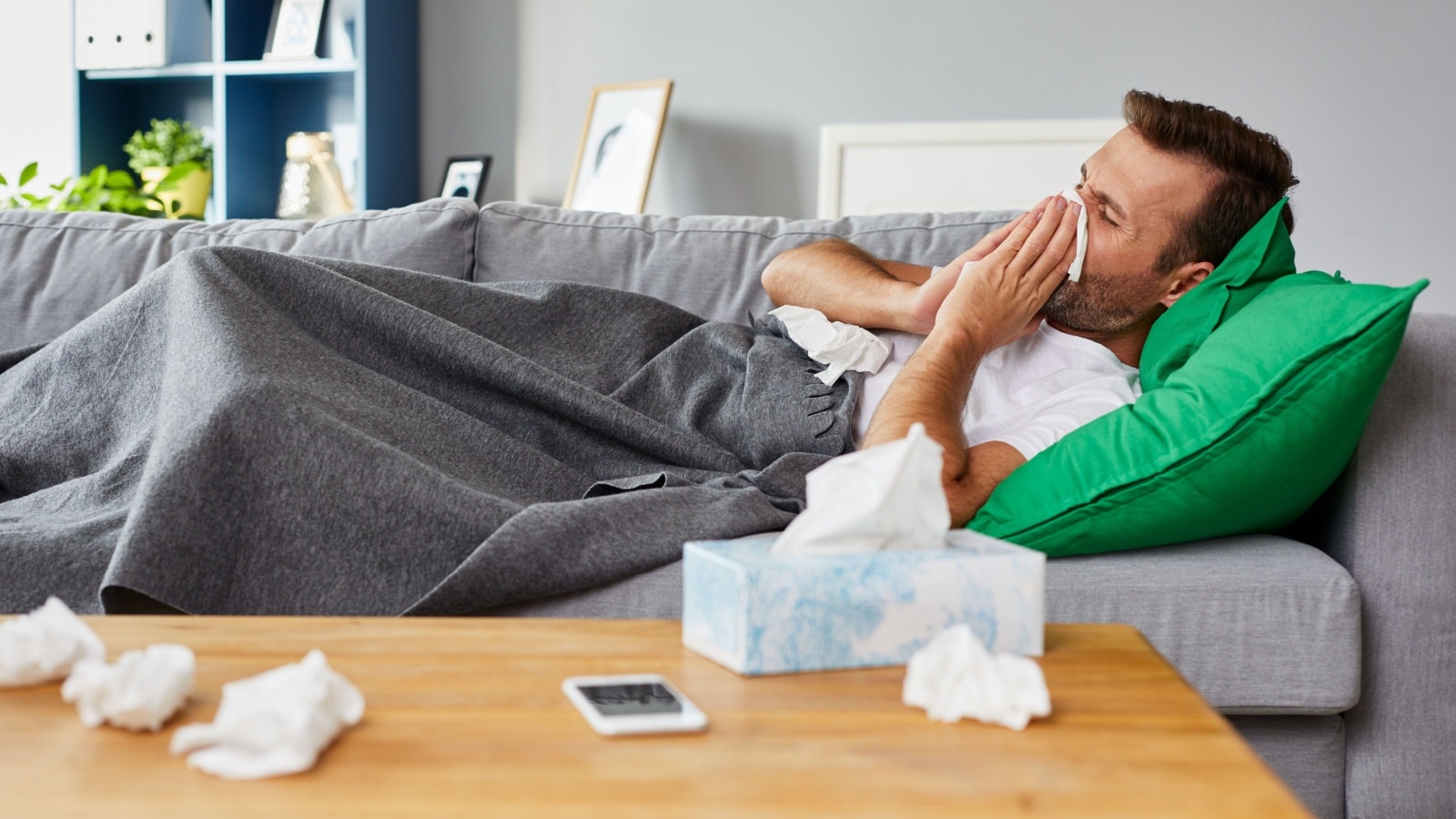 Should I stay home when my partner is sick? A sick man lays on the couch surrounded by tissues.
