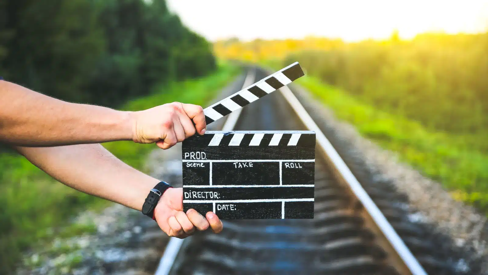 A man holds a clapperboard over train tracks to represent taking action.