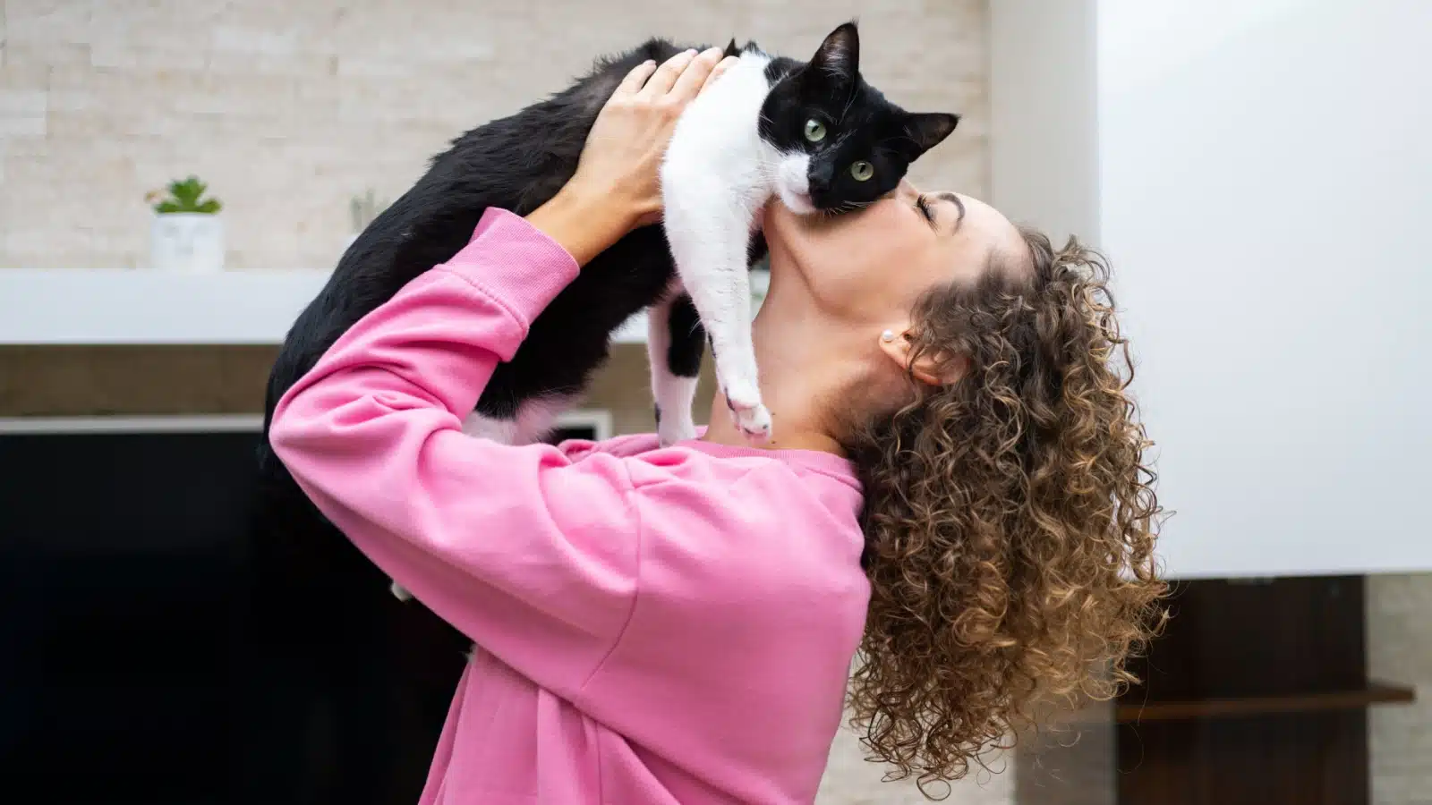 A woman picks up her cat and kisses it. The cat looks disinterested.