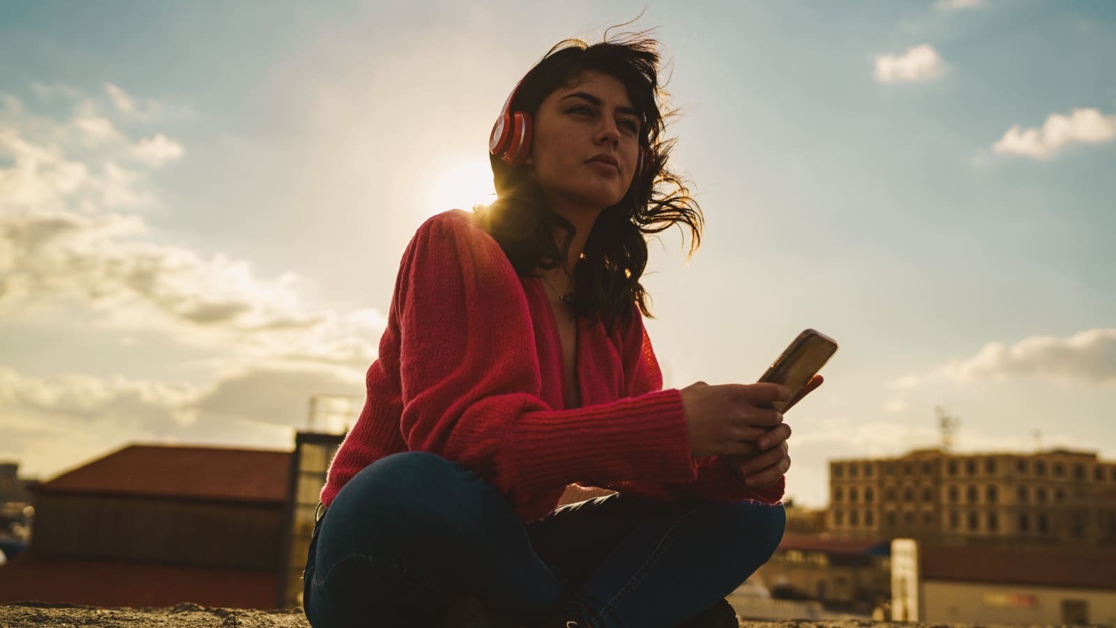 A woman sits alone in an empty lot wearing headphones.